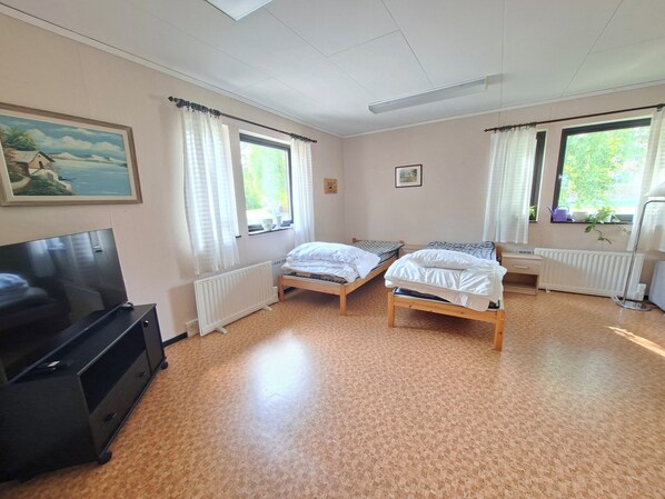A room with two single beds, a television, a radiator, and a window with curtains.