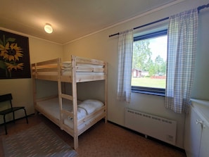 A bunk bed room with a radiator, a window with curtains, a chair, and a sunflower painting.