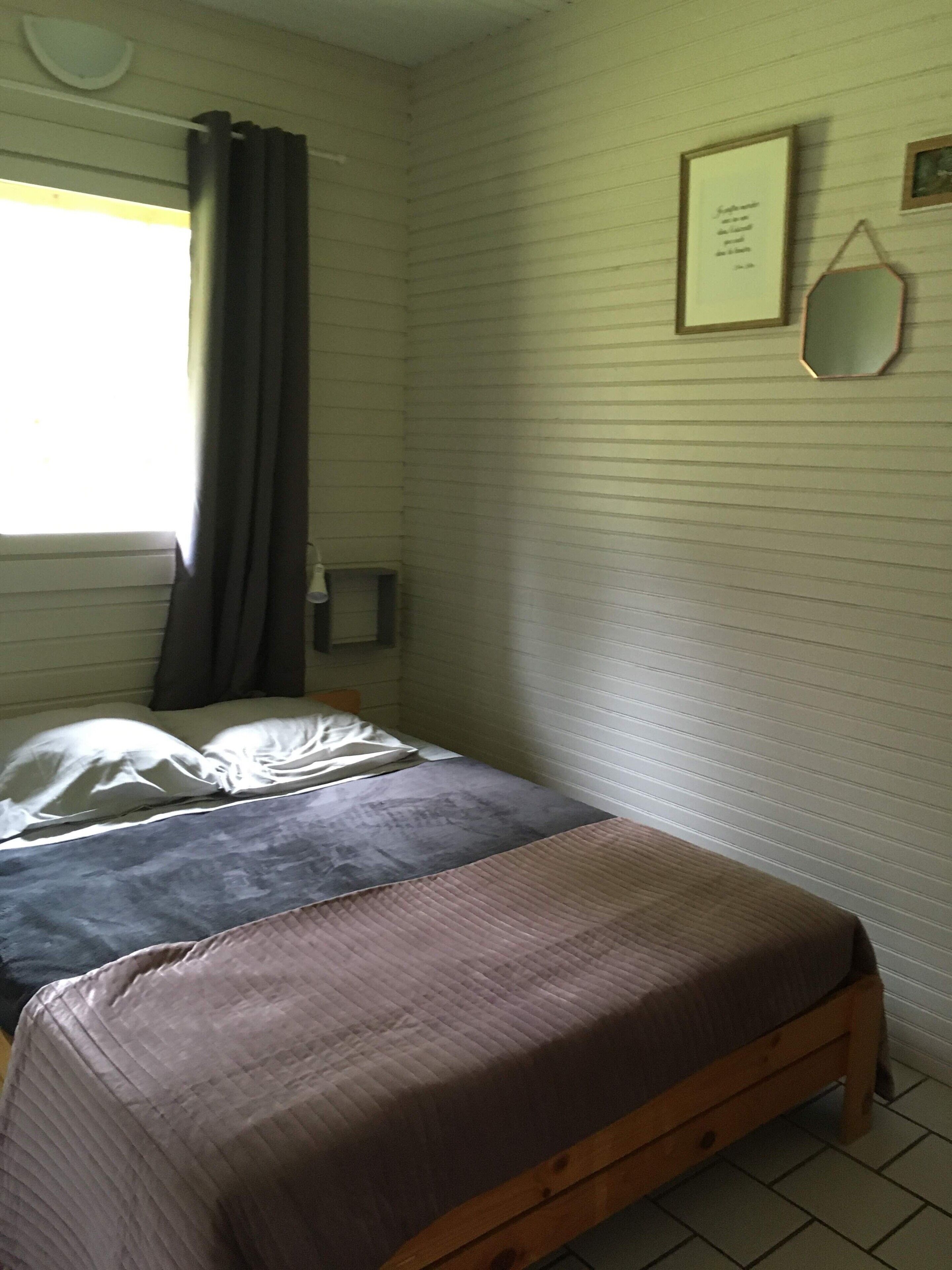 Une chambre à coucher avec un lit, une table de chevet, une fenêtre avec des rideaux et un miroir fixé au mur.