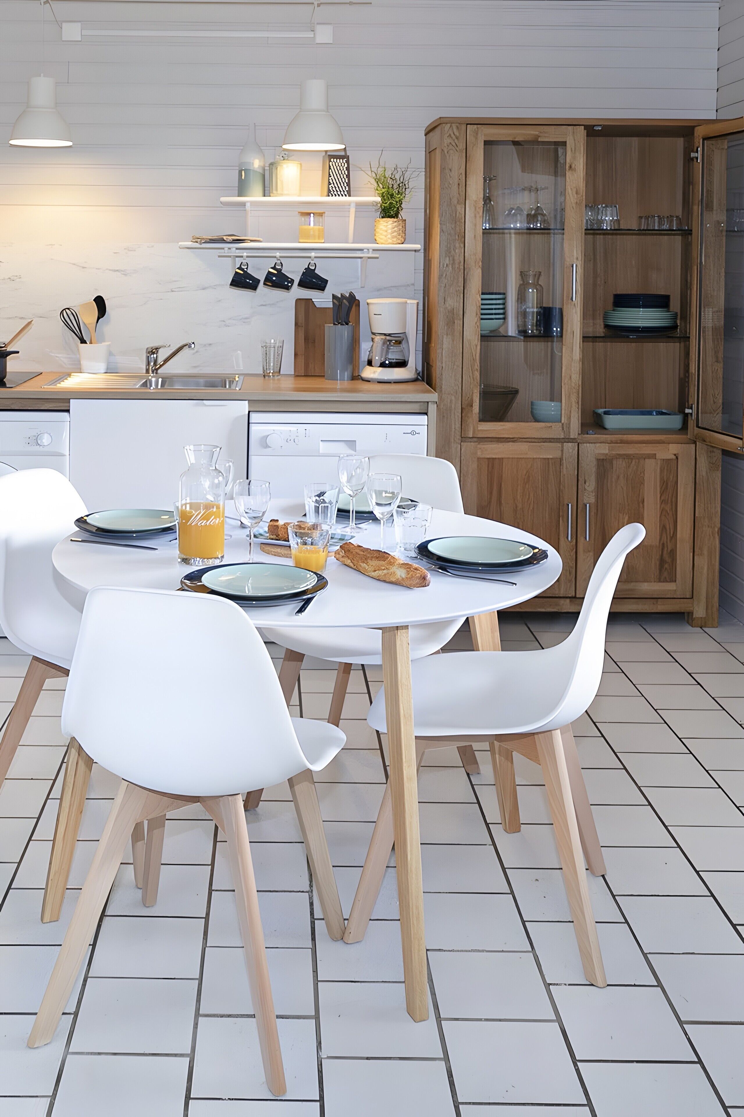Una cocina moderna con armarios blancos, una mesa de comedor dispuesta con platos, vasos y un frutero.