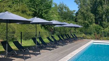 Ein Poolbereich mit Liegestühlen und Sonnenschirmen, umgeben von Bäumen.
