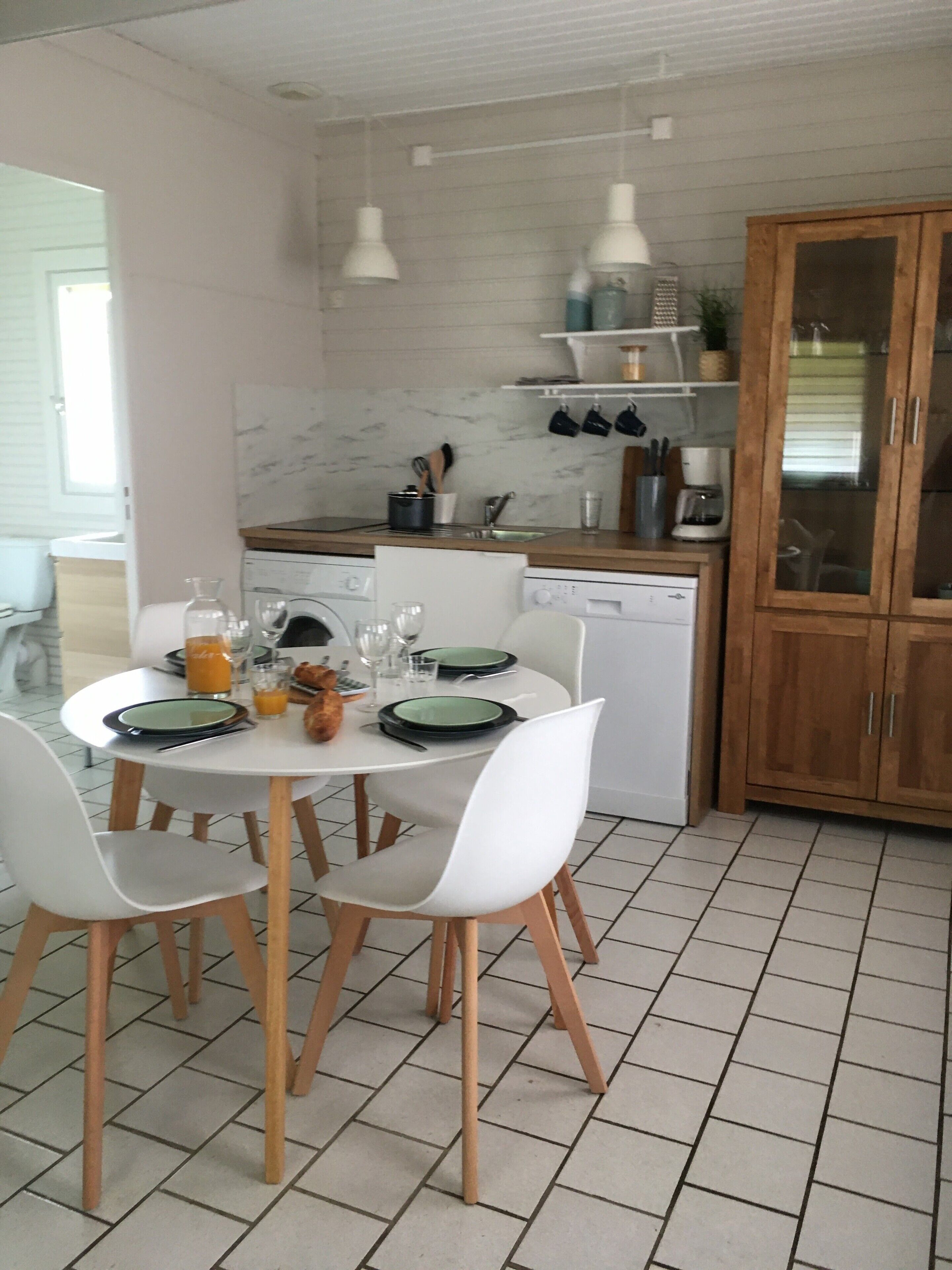 A modern kitchen with white cabinetry, a dining table set for four, and a tiled floor.