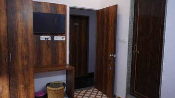 A room with wooden wardrobes, a television, a door, and a tiled floor.