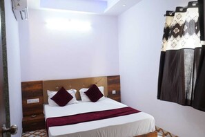 A hotel room with a bed, a nightstand, a wall-mounted air conditioner, and a window with curtains. - Hotel Raj Palace (Udaipur)