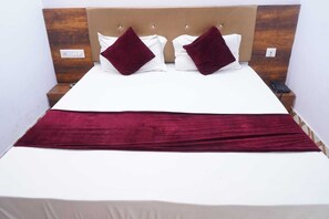A double bed with a wooden headboard, two white pillows, two dark red pillows, a white bedspread, and a red blanket. - Hotel Raj Palace (Udaipur)