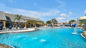 A swimming pool with lounge chairs and umbrellas, surrounded by buildings with tiled roofs. - Wish Upon A Star in Kissimmee (Kissimmee)