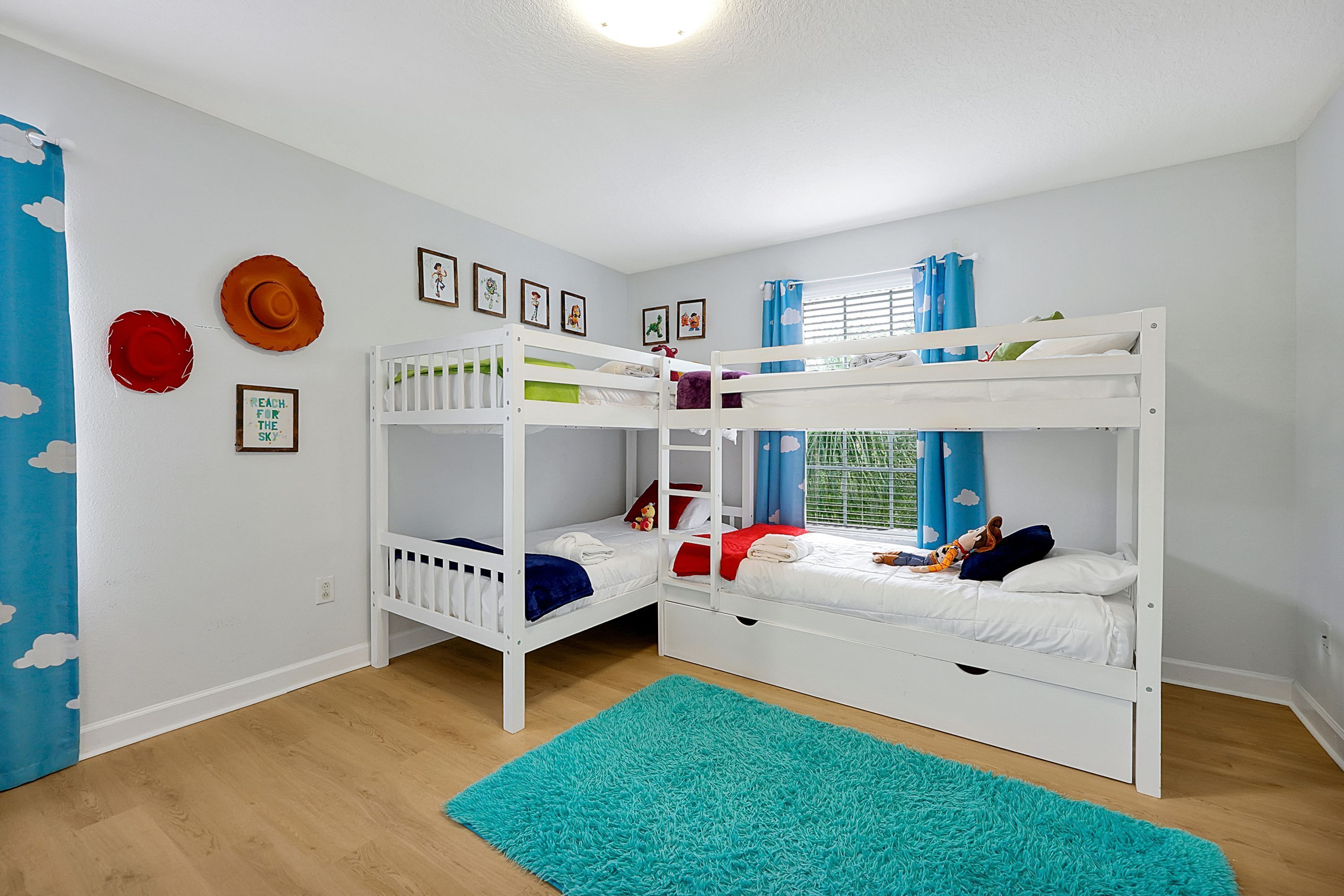 A room with bunk beds, a blue rug, and wall decorations including framed pictures and cloud-patterned curtains.