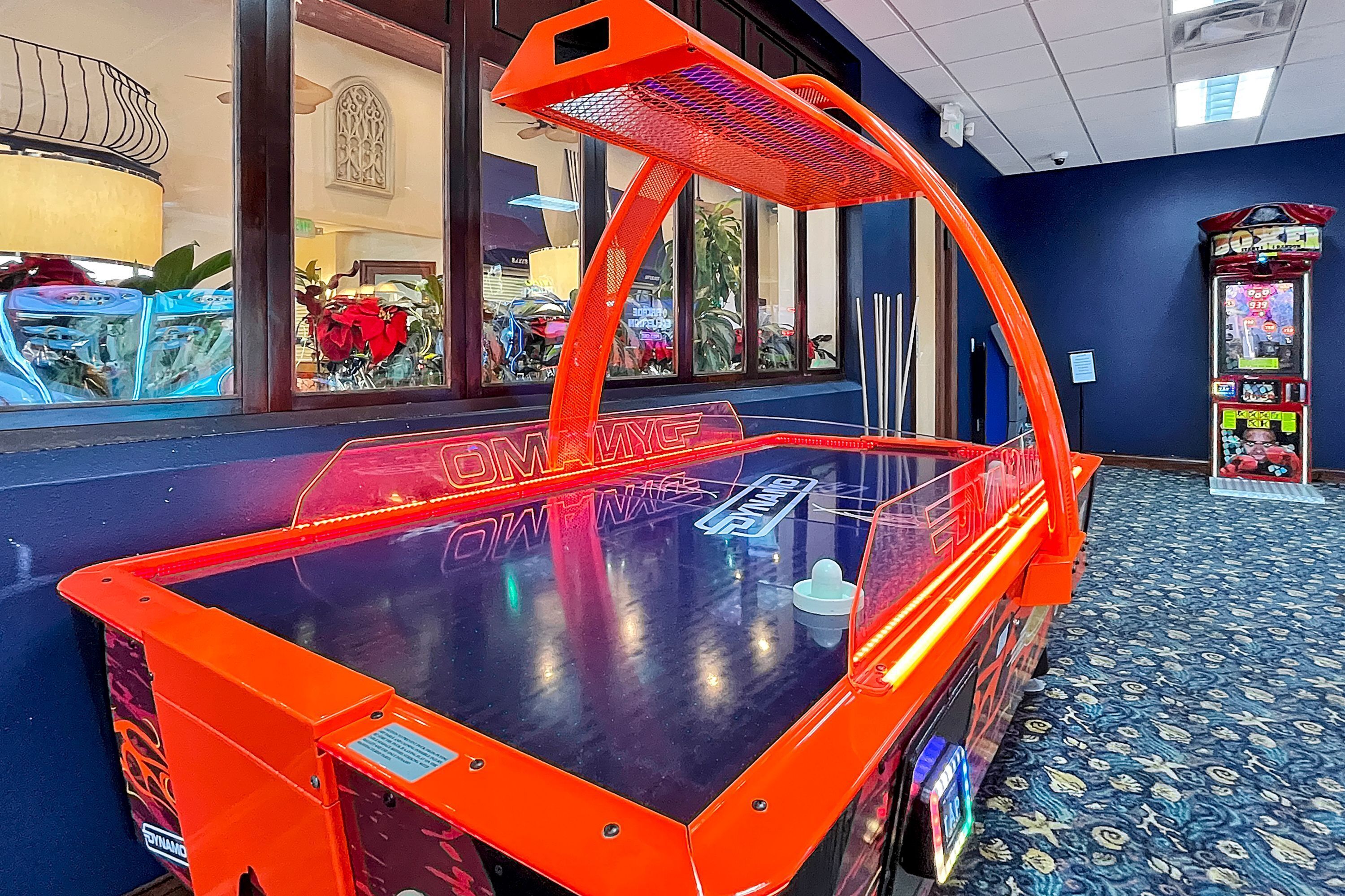 A neon-lit arcade machine with a mirrored surface, located in a room with patterned carpet and a blue wall.