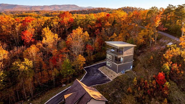 A modern two-story building with a flat roof, surrounded by a forest with autumn foliage, and a winding road nearby. - Skydeck Pinnacle in Sevierville (Sevierville)