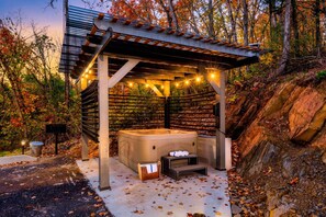 A hot tub under a wooden pergola with string lights, surrounded by autumn foliage. - Skydeck Pinnacle in Sevierville (Sevierville)