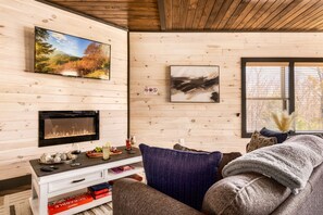Una sala de estar acogedora con chimenea, televisor montado en la pared y una zona de estar cómoda con sofá y cojines.
