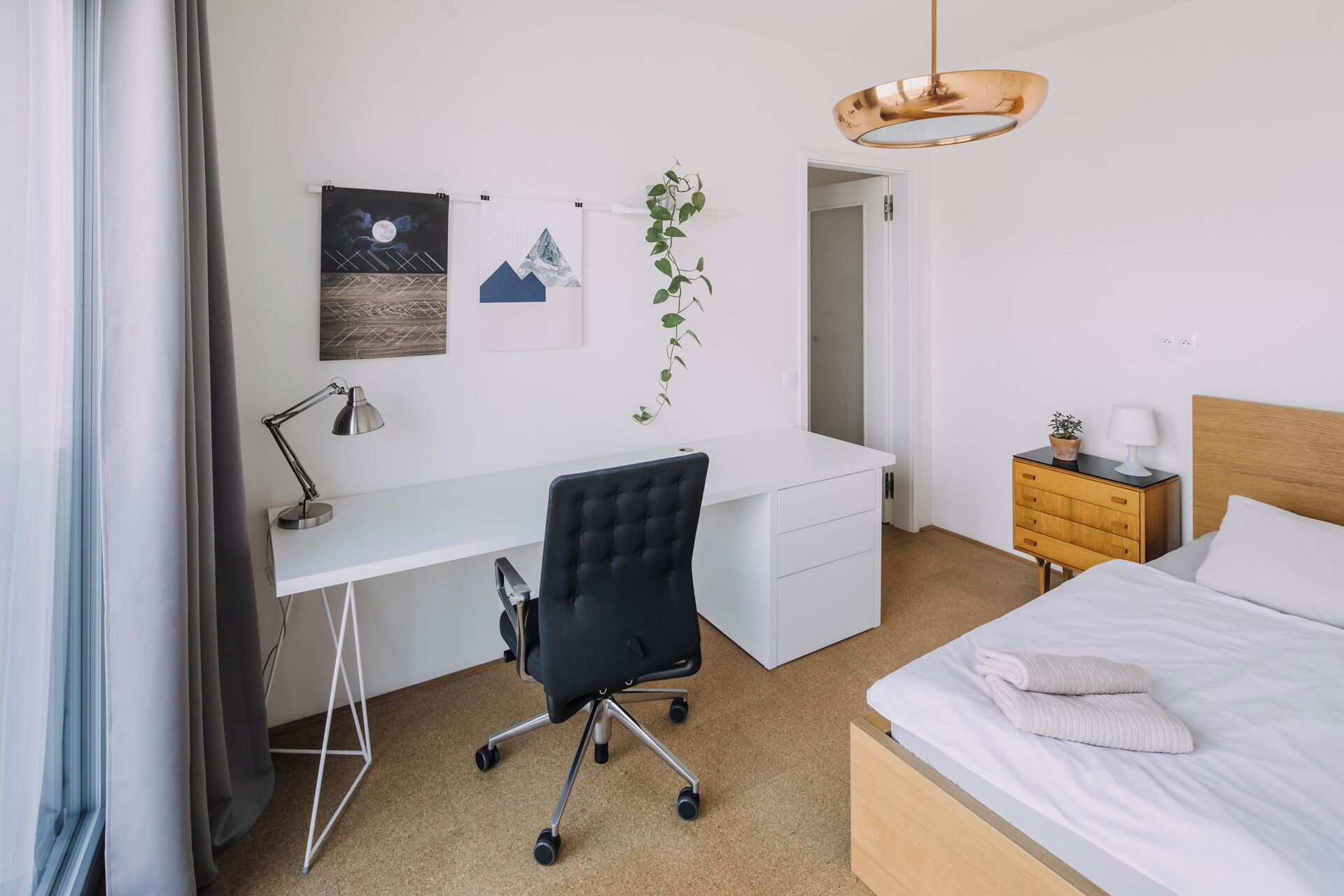 Un dormitorio con cama, escritorio, silla, mesita de noche y lámpara colgante.