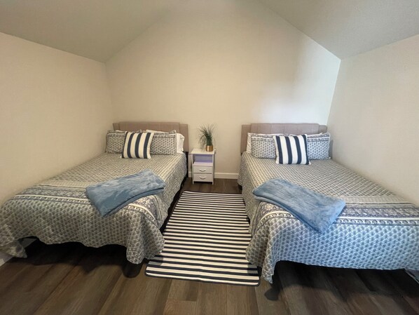 A bedroom with two beds, a nightstand, and a striped rug.