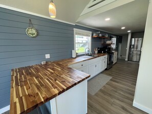 A kitchen with a wooden countertop, white cabinets, a stainless steel refrigerator, and a hanging pendant light.