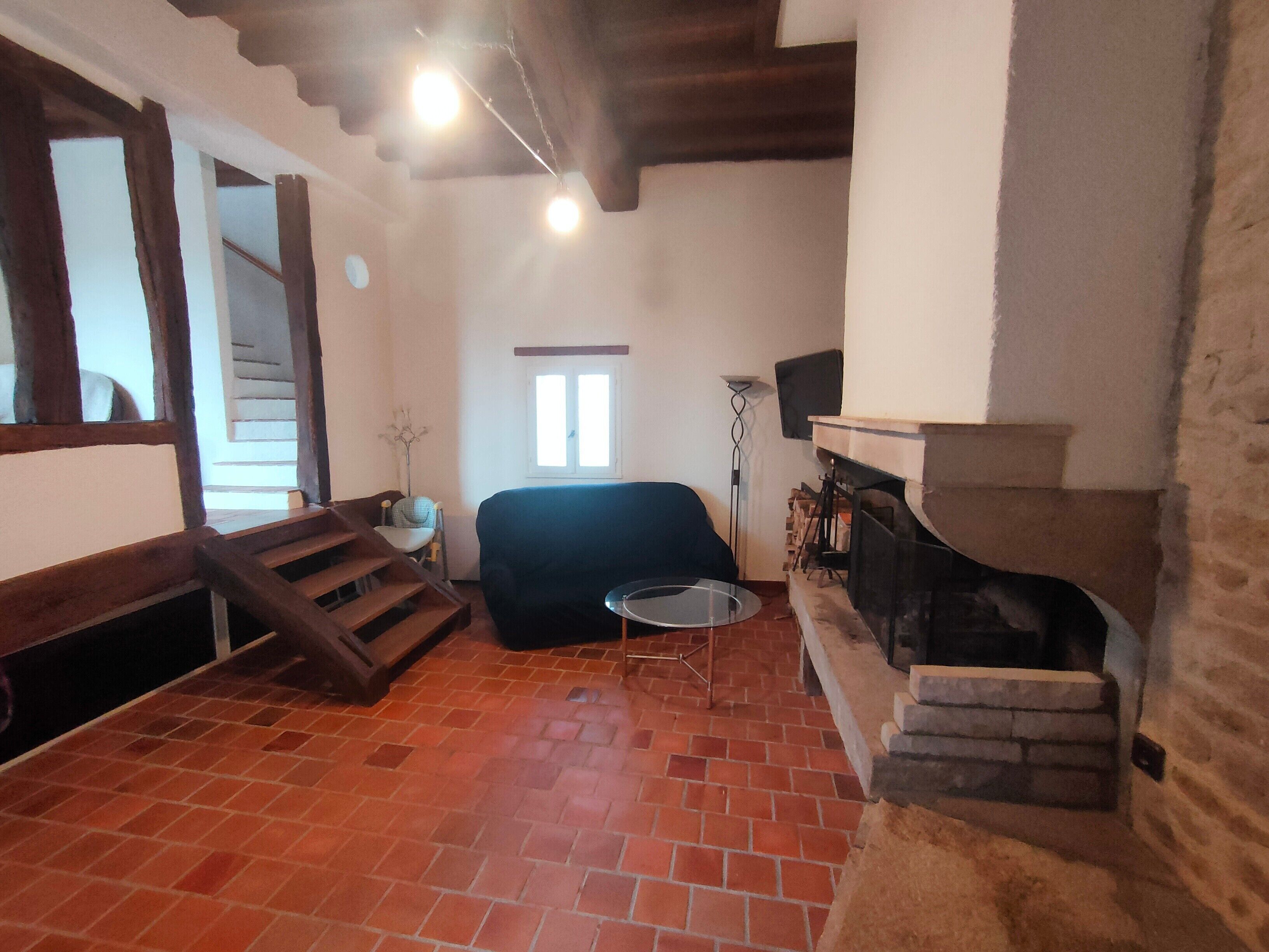 Een kamer met een open haard, een bank, een eettafel en een trap.