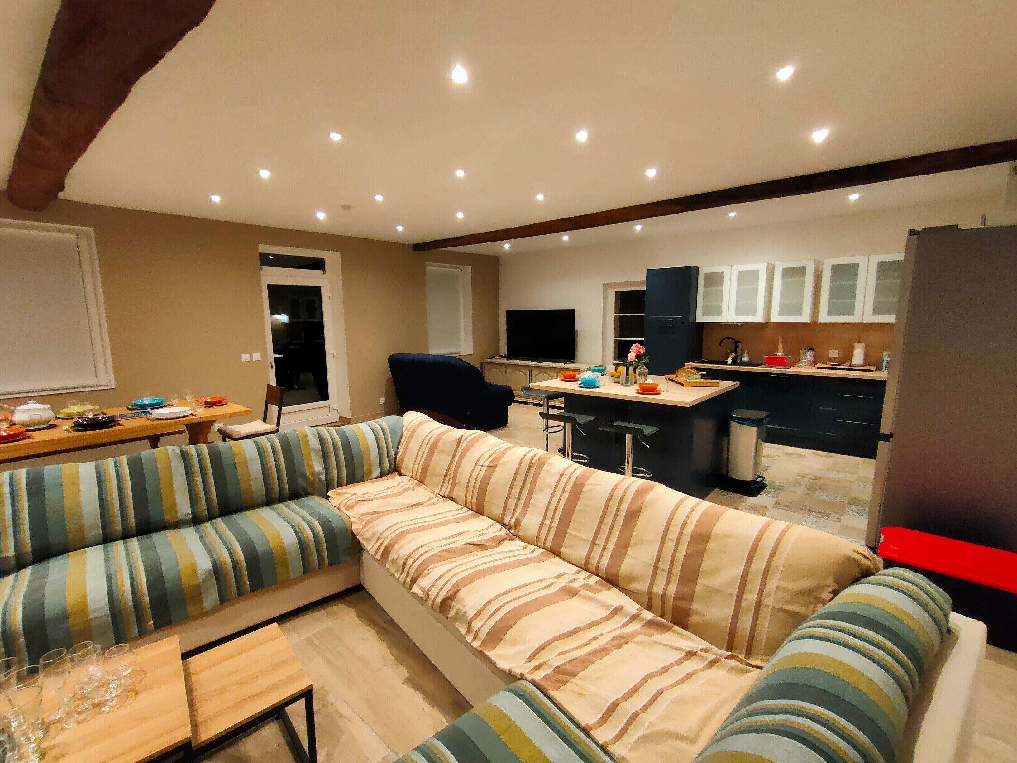 Een moderne woonkamer met een bank, een eettafel en een keukenhoek met kasten en een koelkast.