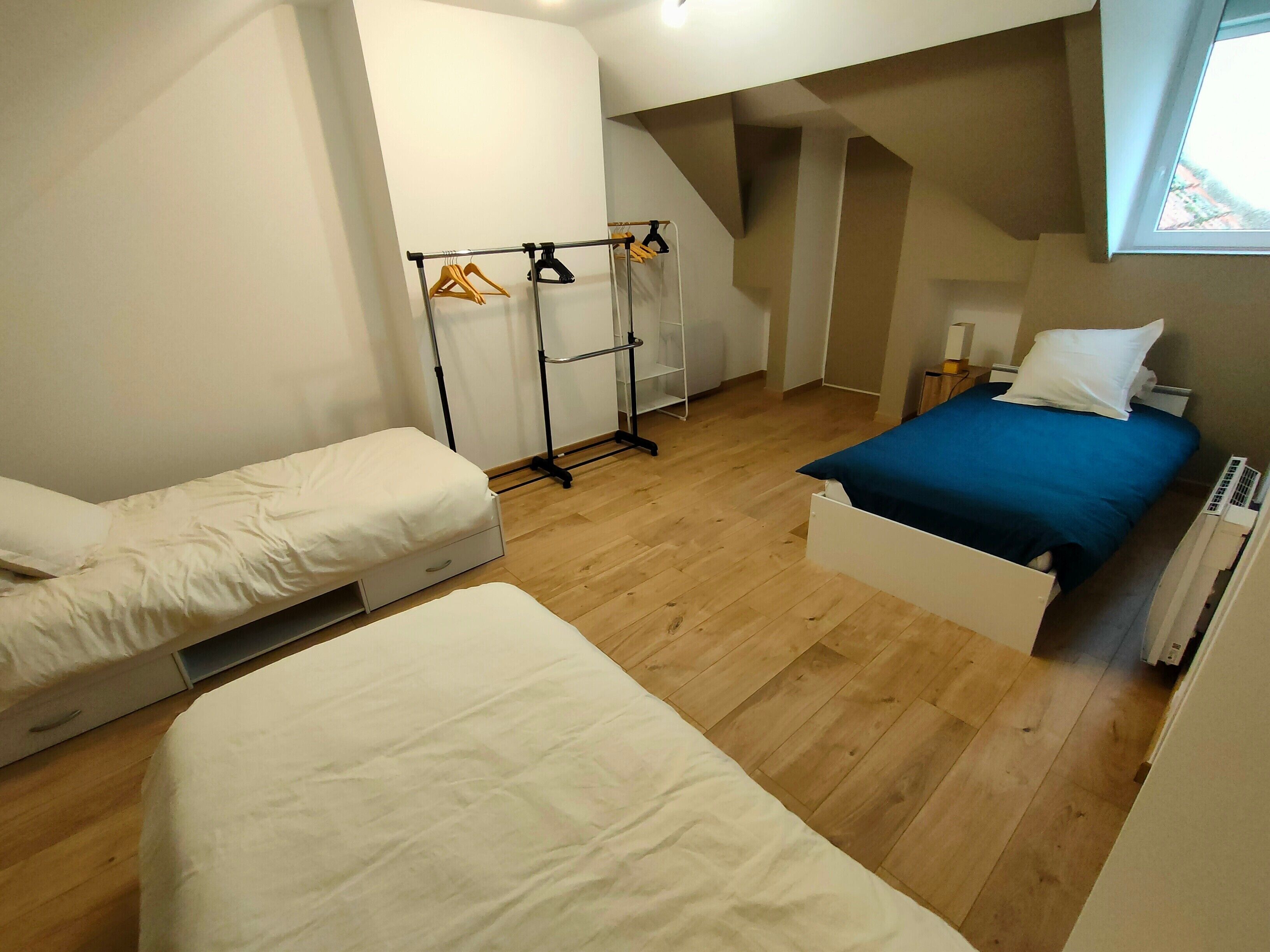 A room with two beds, a radiator, a window, and a clothing rack.