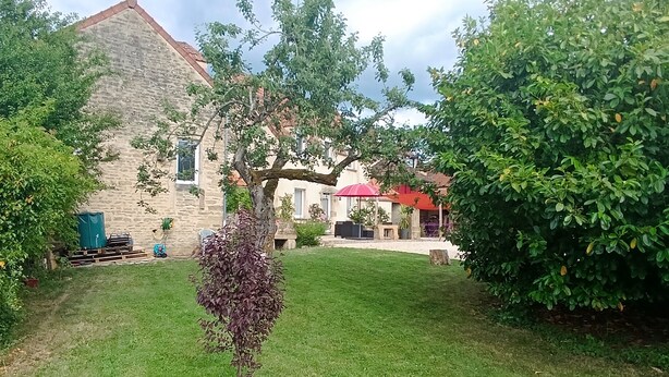 A stone building with a red roof, surrounded by a well-maintained lawn and various trees.