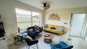 Un salon spacieux avec une grande fenêtre, un canapé, un fauteuil bleu et une table basse.