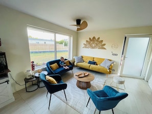 Uma sala de estar ampla com uma grande janela, um sofá, uma poltrona azul e uma mesa de centro.