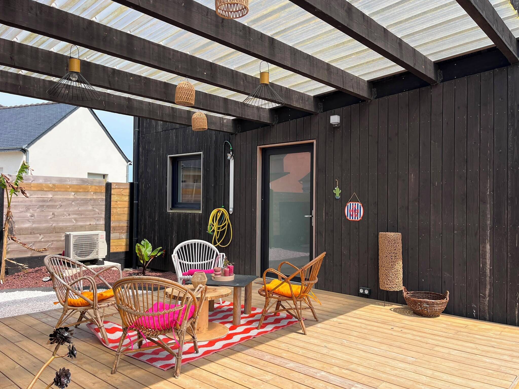 An outdoor patio with wooden flooring, wicker furniture, and a covered area with a metal roof.