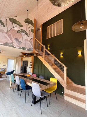 A modern interior with a wooden staircase, a dining area with colorful chairs, and a mural on the wall. - TyGwenHaJu (Plounéour-Brignogan-plages)