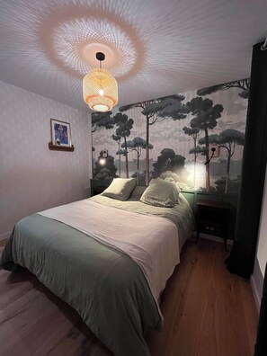 Une chambre à coucher avec un lit, un luminaire suspendu, une fresque murale et une table de chevet.