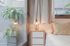 Ein Schlafzimmer mit einem Bett, einem Nachttisch, einer Lampe und zwei Blumentöpfen.