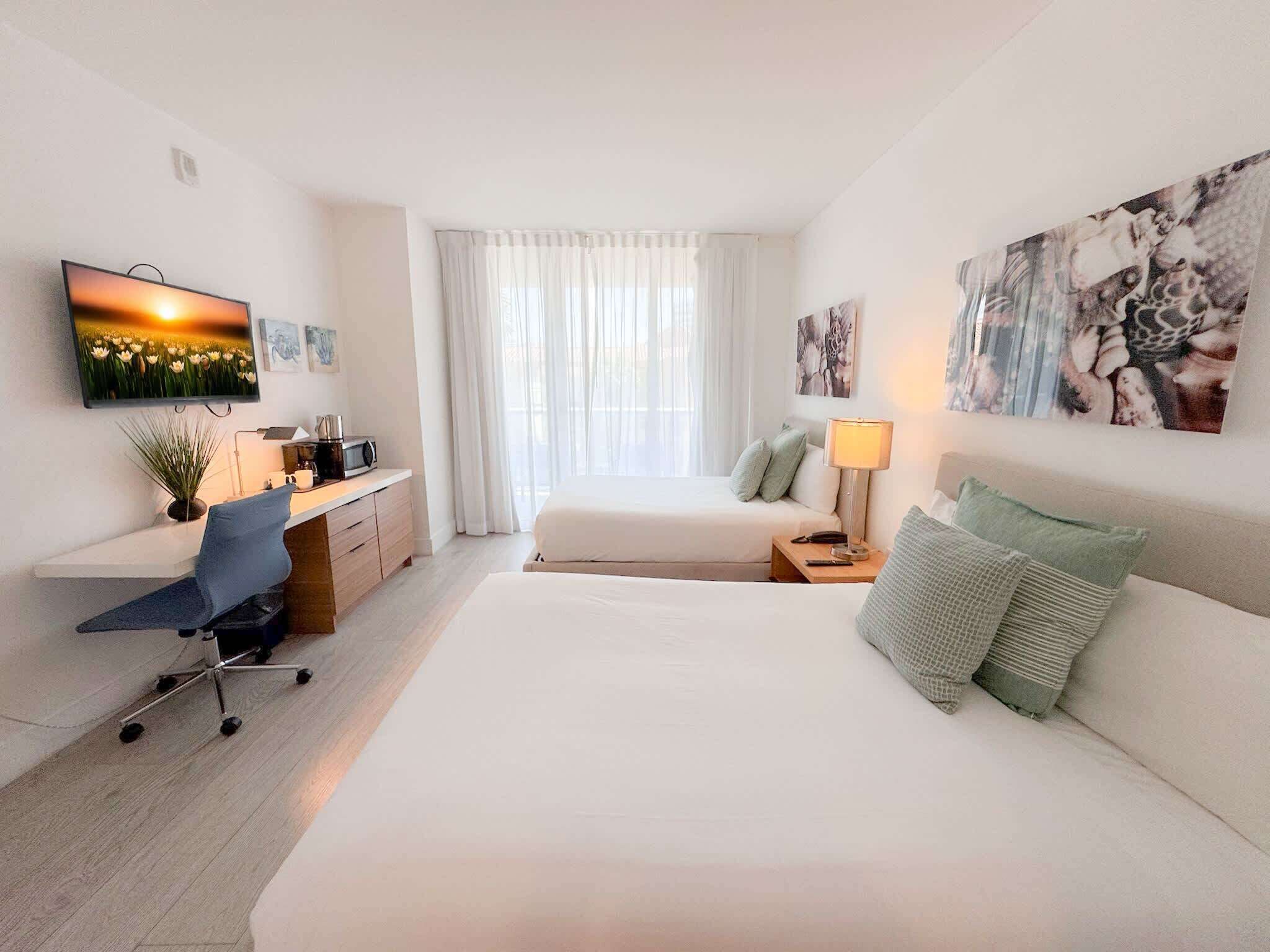 Une chambre d’hôtel équipée d’un lit, d’un bureau avec une chaise, d’une télévision et d’œuvres d’art accrochées aux murs.