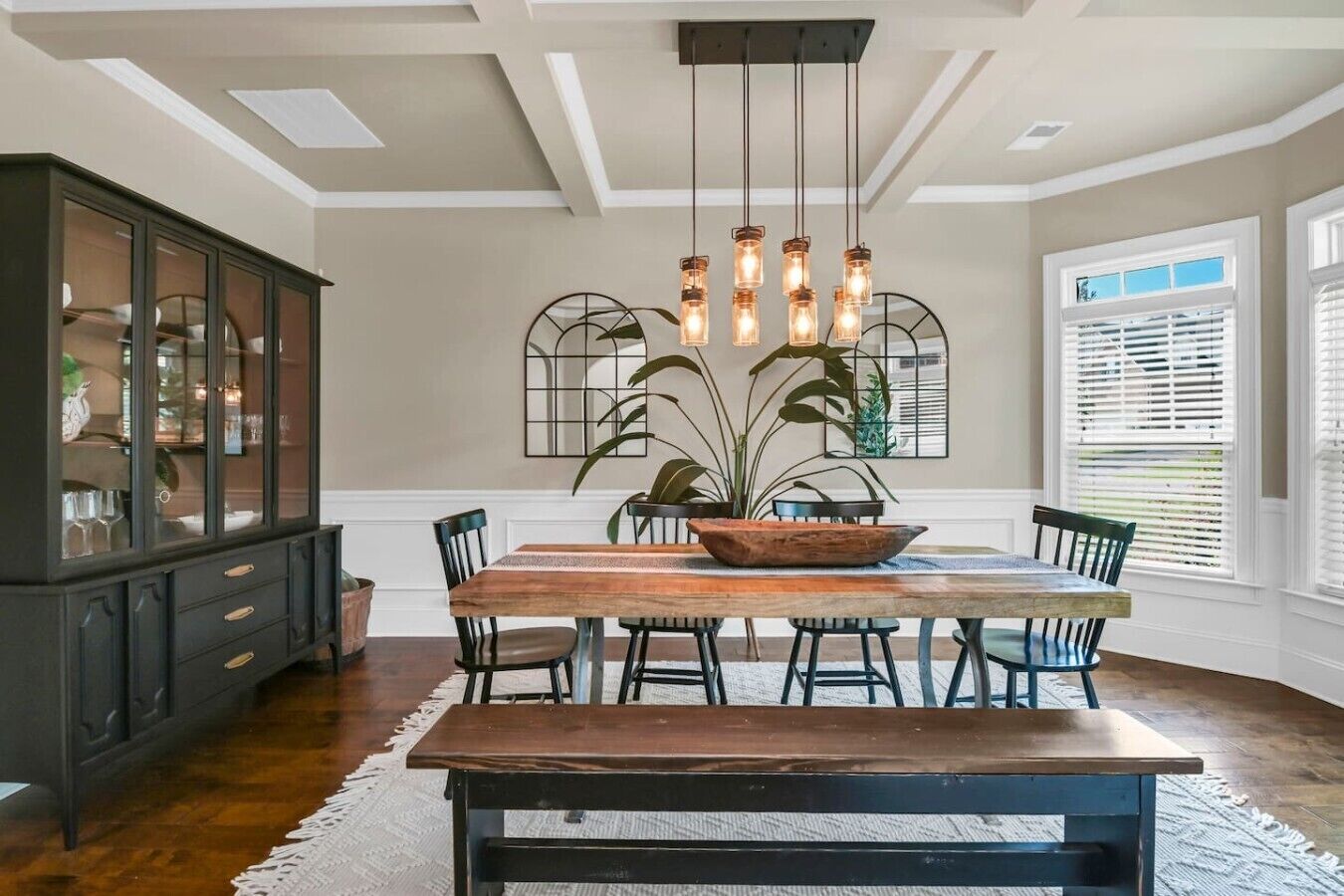 A dining area with a wooden table, chairs, a dark wooden cabinet, and a hanging light fixture.