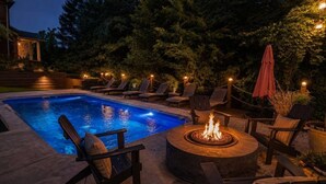Una piscina con sillones de descanso y zona con fogata.