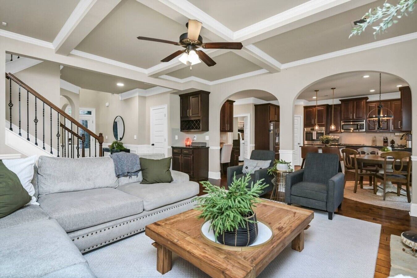 A spacious living room with a large sofa, a coffee table with a plant, and a ceiling fan.