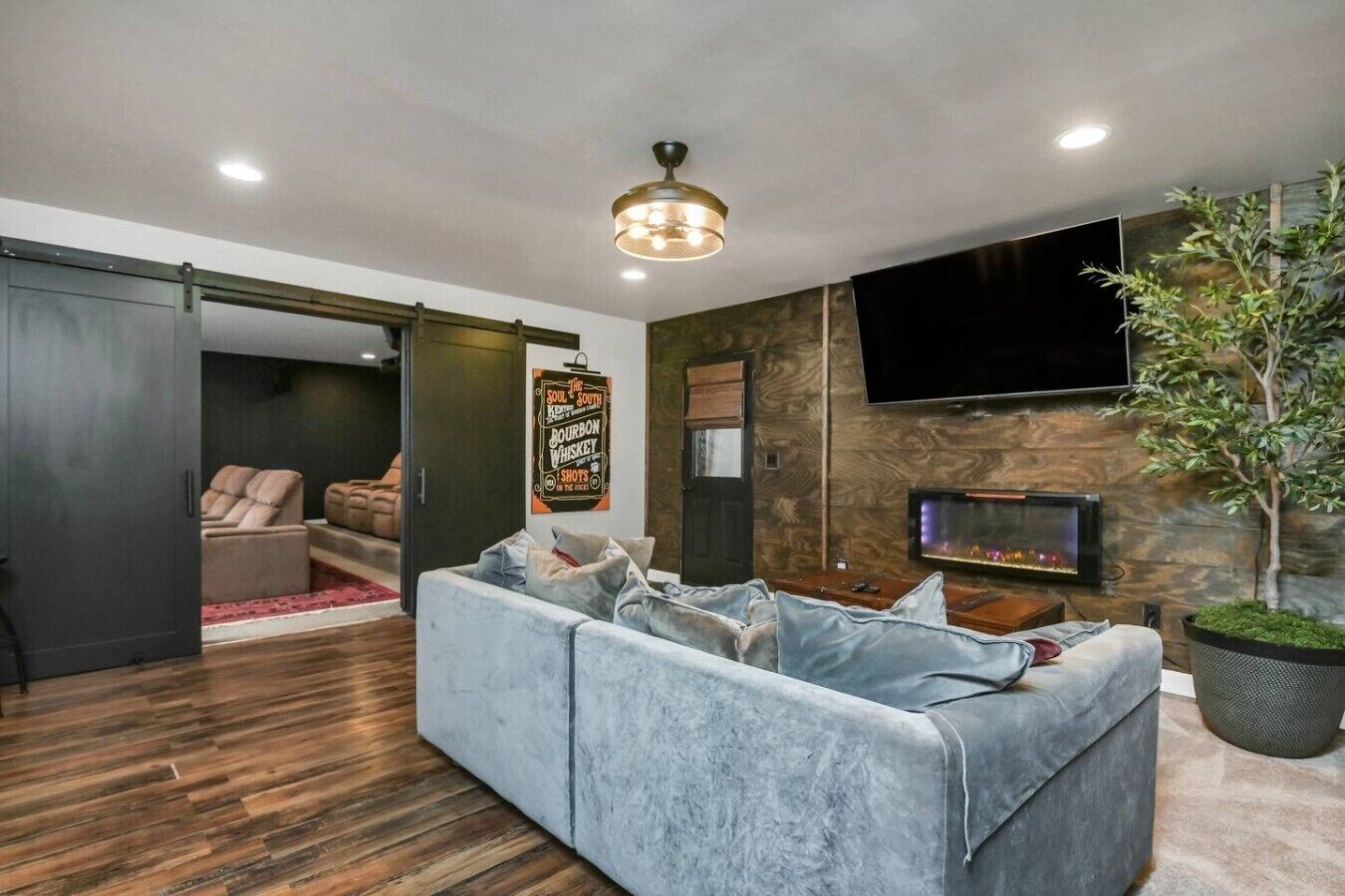 A modern living room with a grey sofa, a flat-screen TV, a fireplace, and a large plant.
