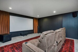 A home theater room with a large screen, reclining seats, a speaker, and a carpet. - Luxury Chapin Retreat | Pool, Theater, Gym + Bar (Chapin)