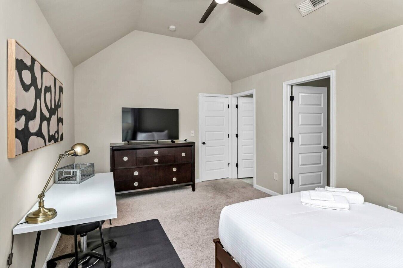 Een slaapkamer met een bed, een bureau met lamp, een dressoir, een televisie en twee kasten.