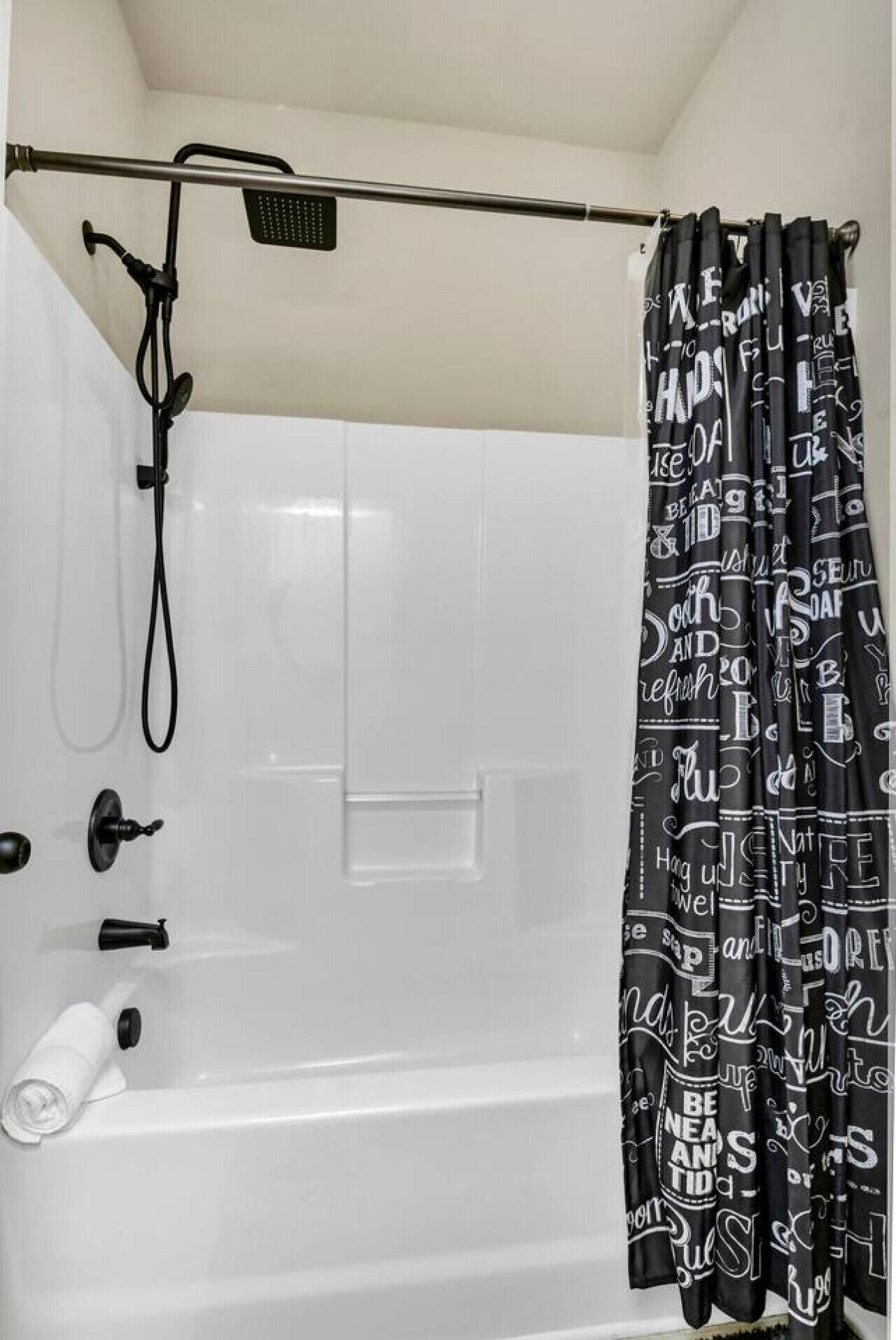 Ein Badezimmer mit einer weißen Badewanne, einem Duschvorhang mit Schriftzug und einer Handbrause.