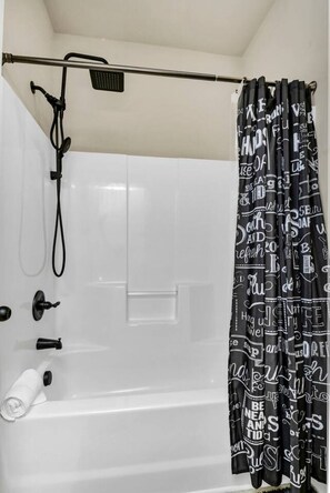 A bathroom with a white bathtub, a shower curtain with text, and a handheld showerhead. - Luxury Chapin Retreat | Pool, Theater, Gym + Bar (Chapin)