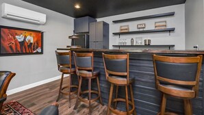 Una cocina moderna con barra, que incluye taburetes de madera, un refrigerador y un cuadro en la pared.