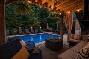 An outdoor pool area with lounge chairs, a sofa, and a table, surrounded by greenery and string lights. - Luxury Chapin Retreat | Pool, Theater, Gym + Bar (Chapin)