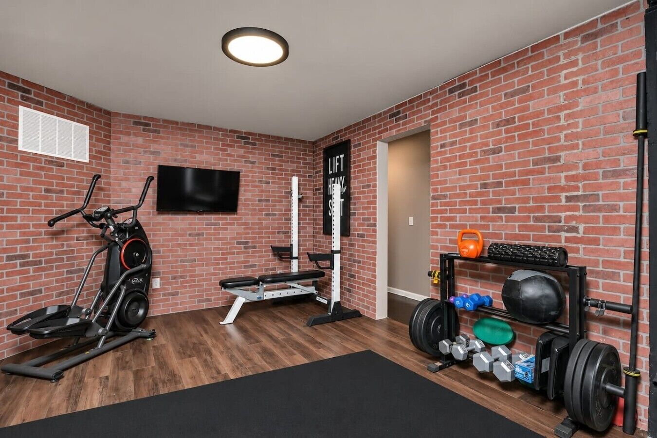 Een huisgymnasium met een hometrainer, een bankdrukrek, kettlebells en een televisie bevestigd aan de bakstenen muur.