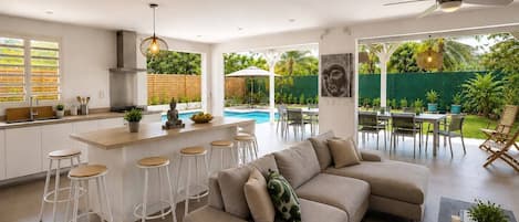 Una cocina moderna con barra, un comedor con mesas al aire libre y una piscina.