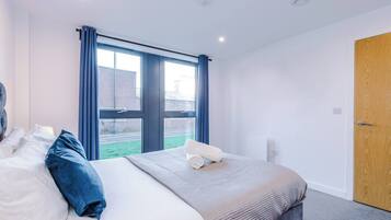 Quarto de hotel com uma cama grande, janela com cortinas, porta de madeira e vista para o exterior.