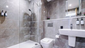 A modern bathroom with a glass-enclosed shower, a white toilet, and a sink with toiletries. - #82 Stylish Shirley Home Sleeps 8 NEC Solihull BHX (Shirley)