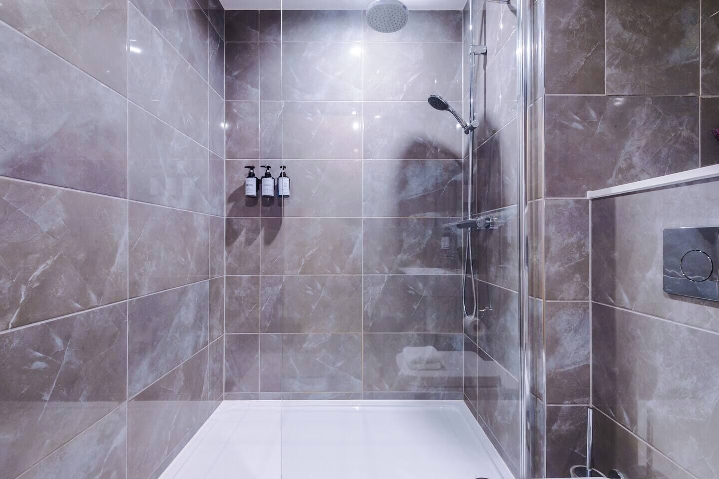 Uma casa de banho moderna com cabine de chuveiro em vidro, azulejos de mármore e chão branco.