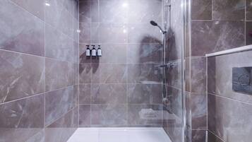 Uma casa de banho moderna com cabine de chuveiro em vidro, azulejos de mármore e chão branco.