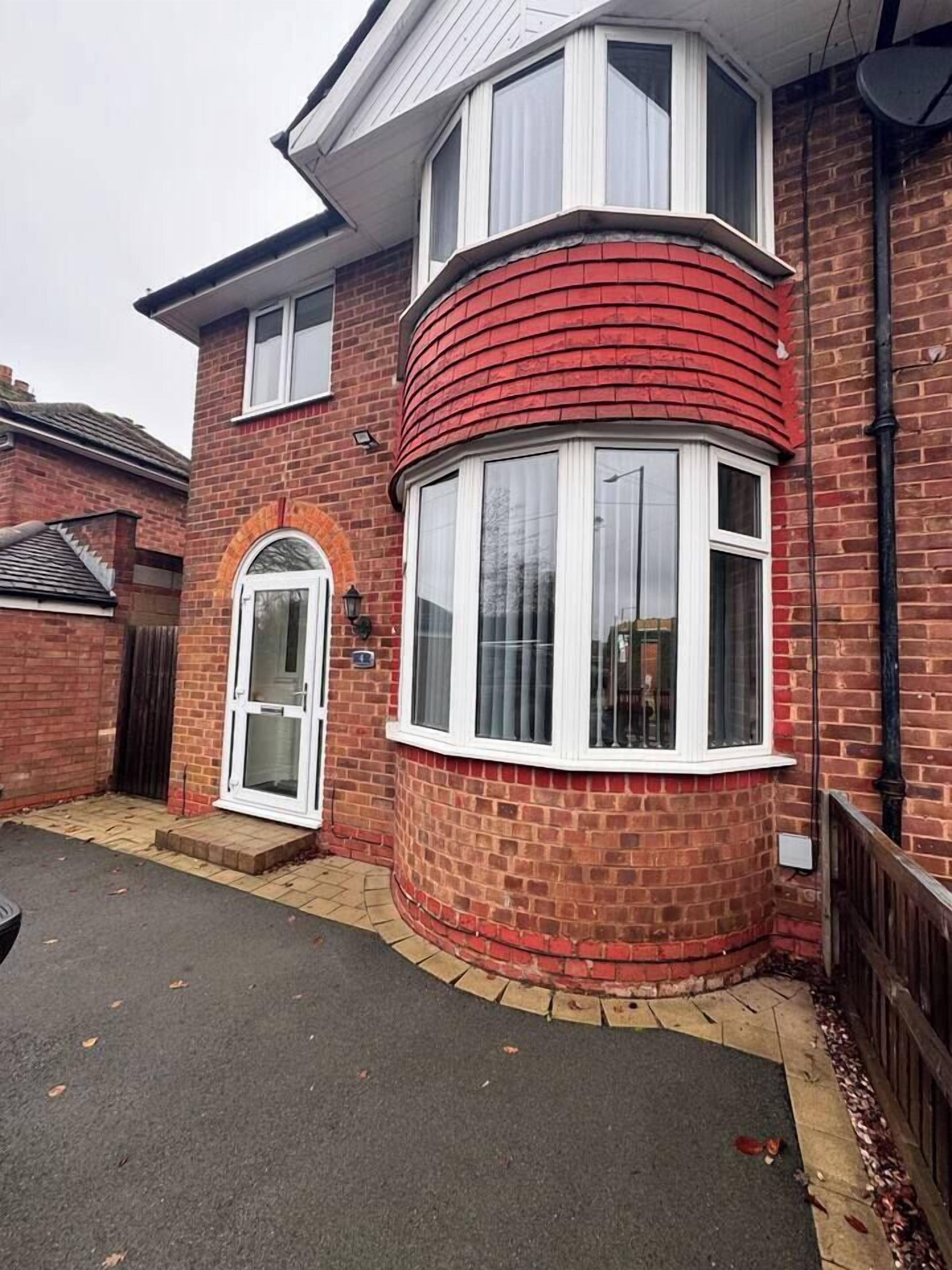 Une maison à deux étages avec une façade en briques rouges, une baie vitrée et une porte blanche.