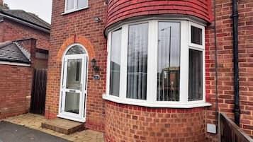 Une maison à deux étages avec une façade en briques rouges, une baie vitrée et une porte blanche.