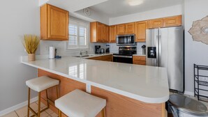 A modern kitchen with wooden cabinets, a large island with stools, a stainless steel refrigerator, and a microwave. - Seaside Beach & Racquet 3801 (Orange Beach)