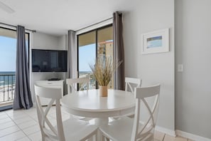A room with a balcony, a dining table with chairs, a TV, and a framed picture on the wall. - Seaside Beach & Racquet 3801 (Orange Beach)