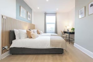 A modern bedroom with two beds, a desk, and a large window. - Spacious 2BR Near Leeds Centre – Free Parking (Leeds)